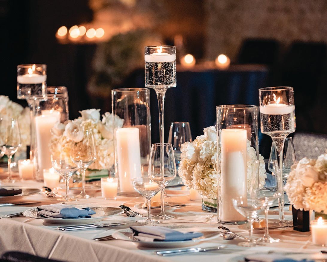 Varying-height glass cylinders and stemmed candle cups accented the tables
