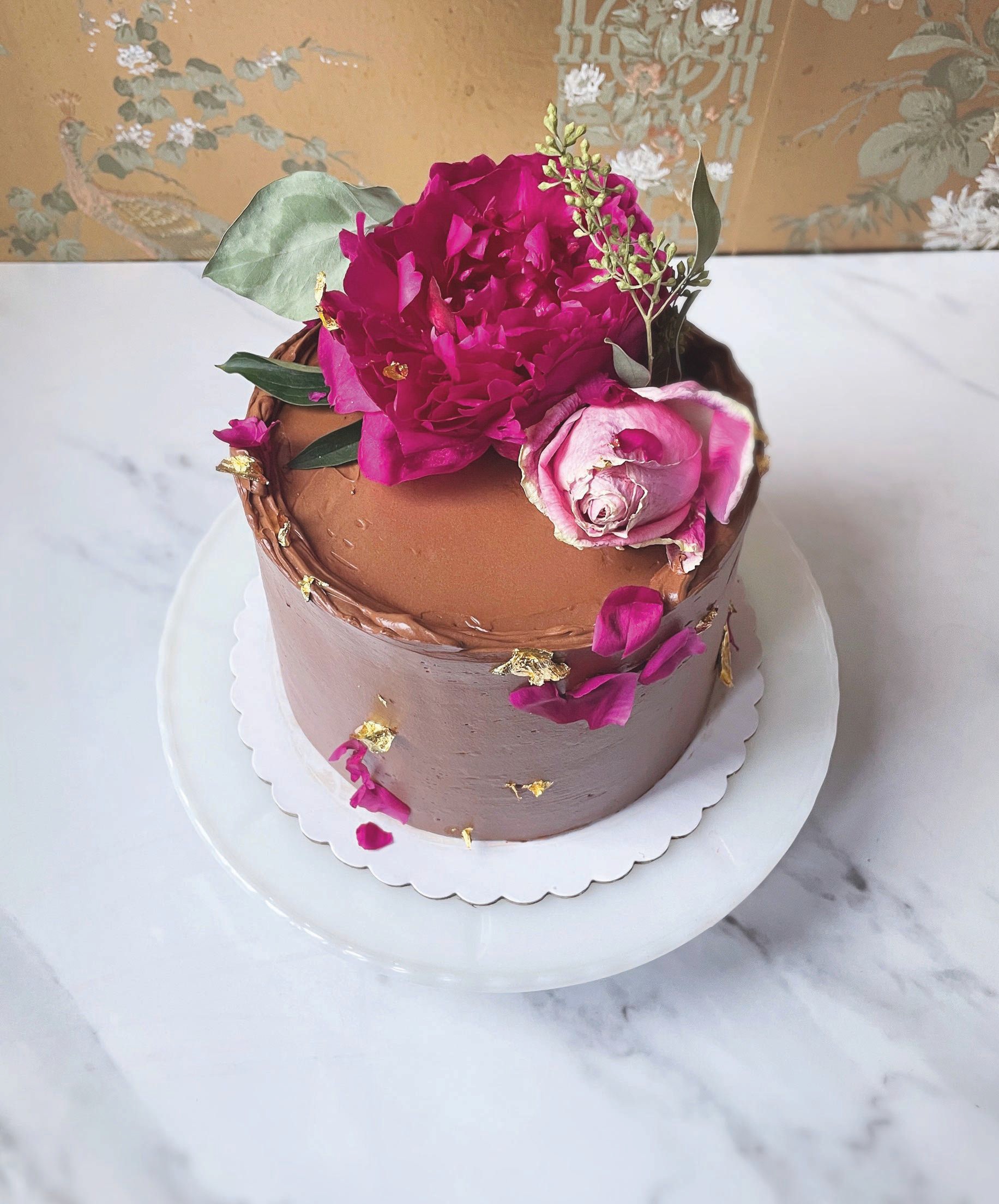 A blooming rose, petals, greenery and gold leaf sprinkle the top of this festive gateau. PHOTO BY NOELLE BLIZZARD